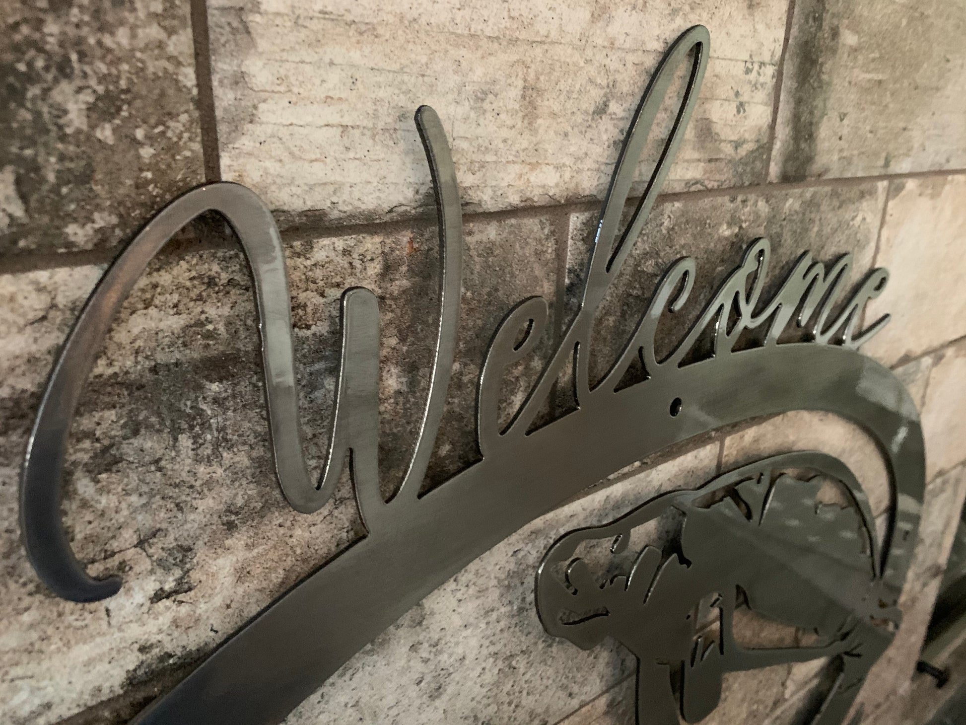 Closeup of welcome written on the top of brushed metal  3 manatee sign with clear powder coat